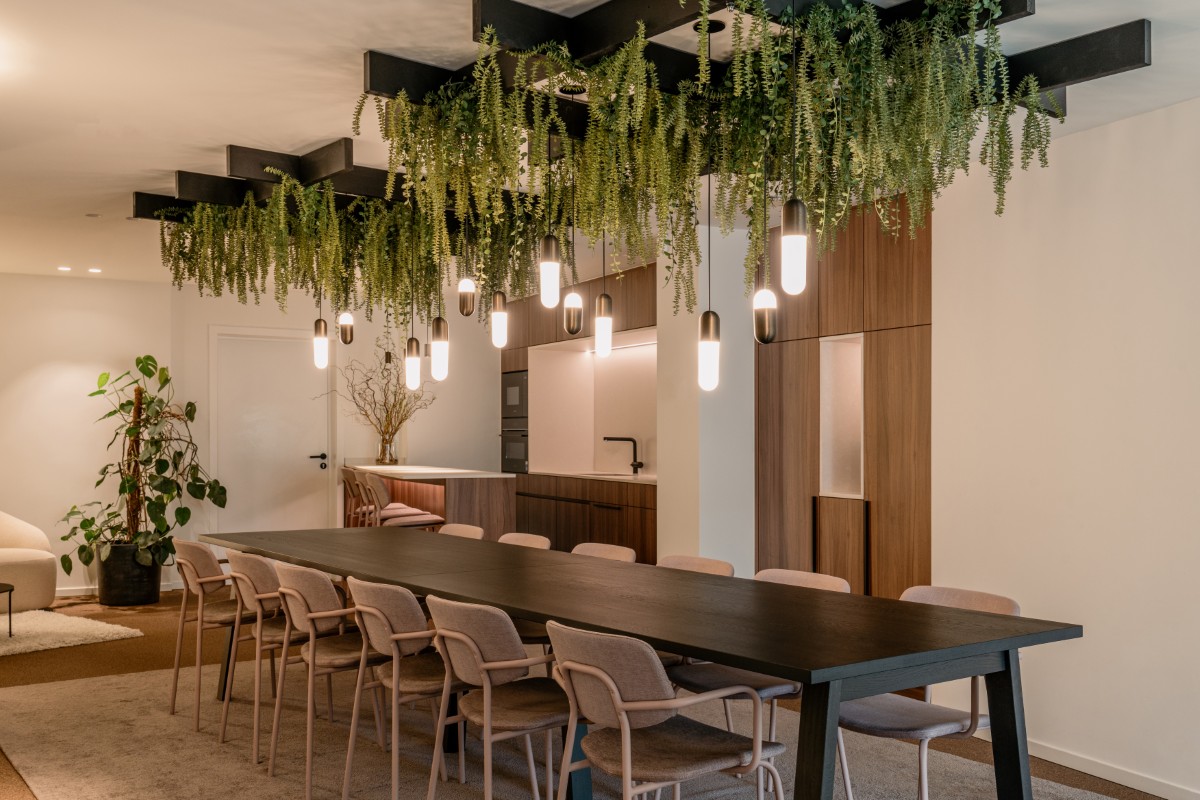 Overzicht eetzaal met lange tafel, hanglampen en hangende planten aan het plafond, kantoorinrichting AJO door Homescape. Foto: Hannelore Veelaert